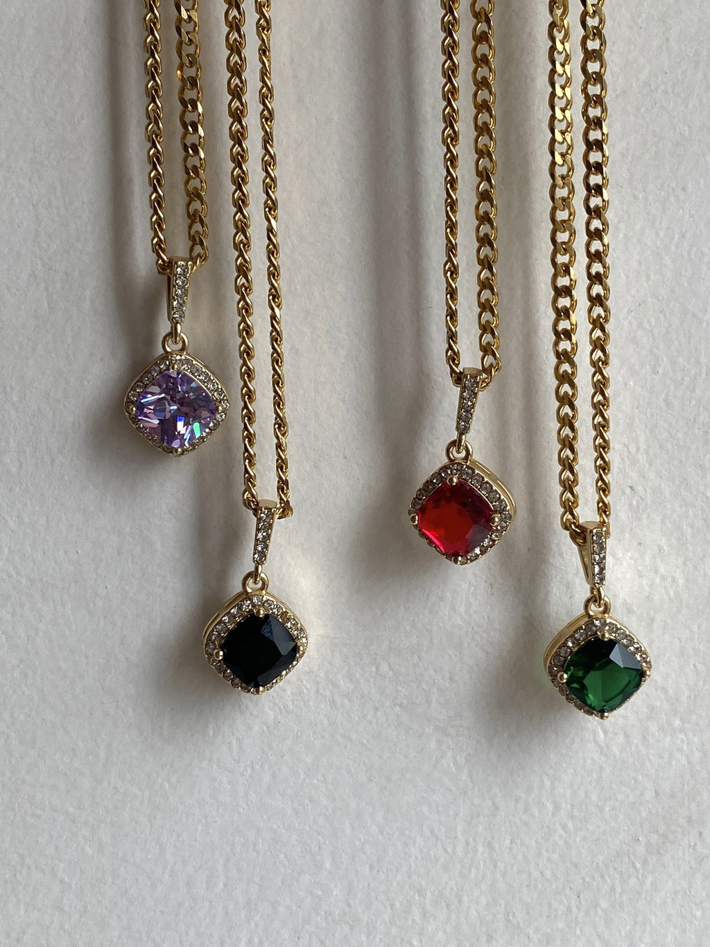 Four gold necklaces with colored gemstones on a white background