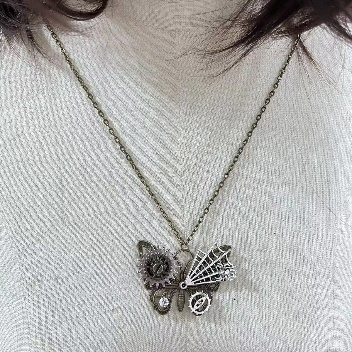 Necklace with a butterfly pendant featuring gears and a spider web on a light fabric background.