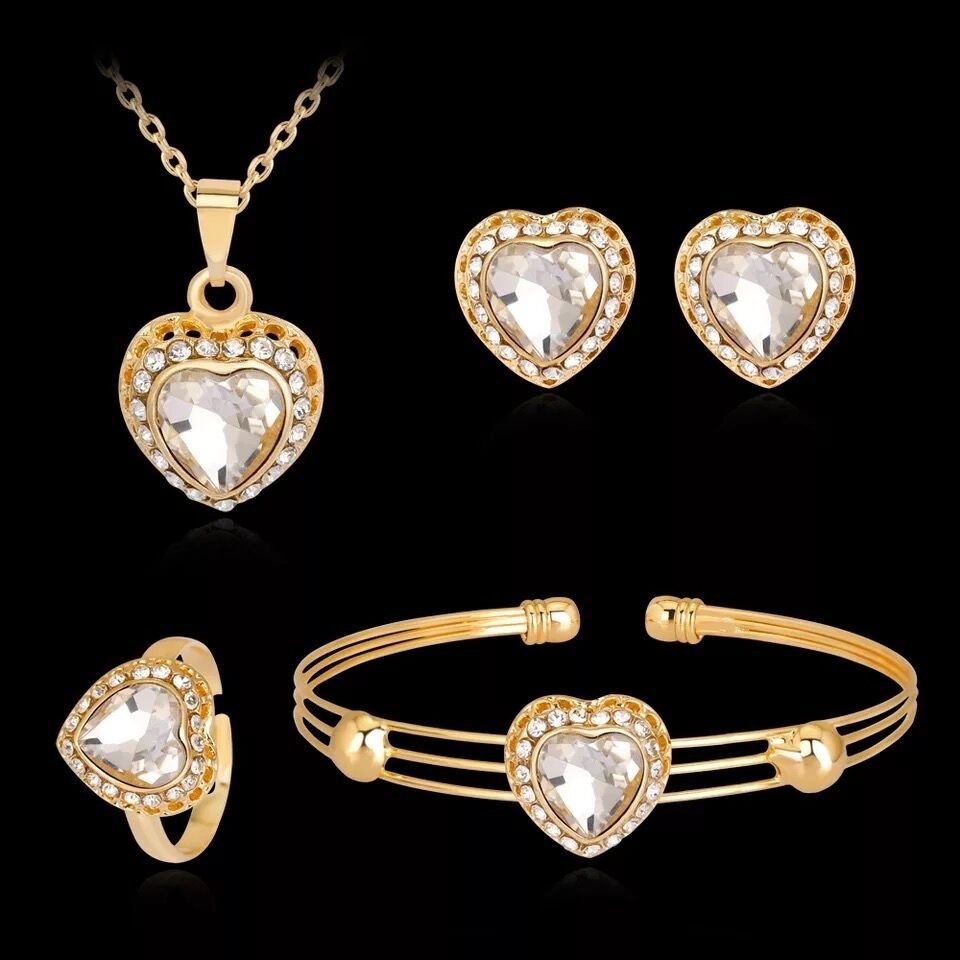 Gold heart-shaped jewelry set with necklace, earrings, ring, and bracelet on a black background
