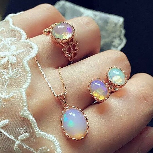 Rose gold jewelry set with opal stones on a hand wearing a lace glove.