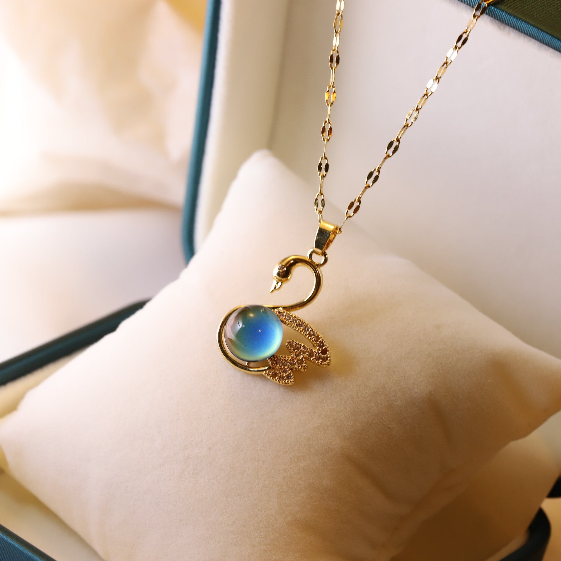 Gold swan necklace with a blue gemstone on a white cushion