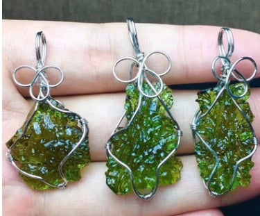 Three green leaf-shaped pendants on silver wires held in a hand.