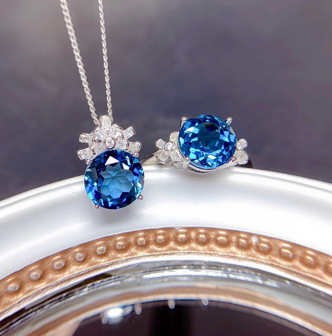 Blue gemstone necklace and earrings on a reflective surface with a blurred background