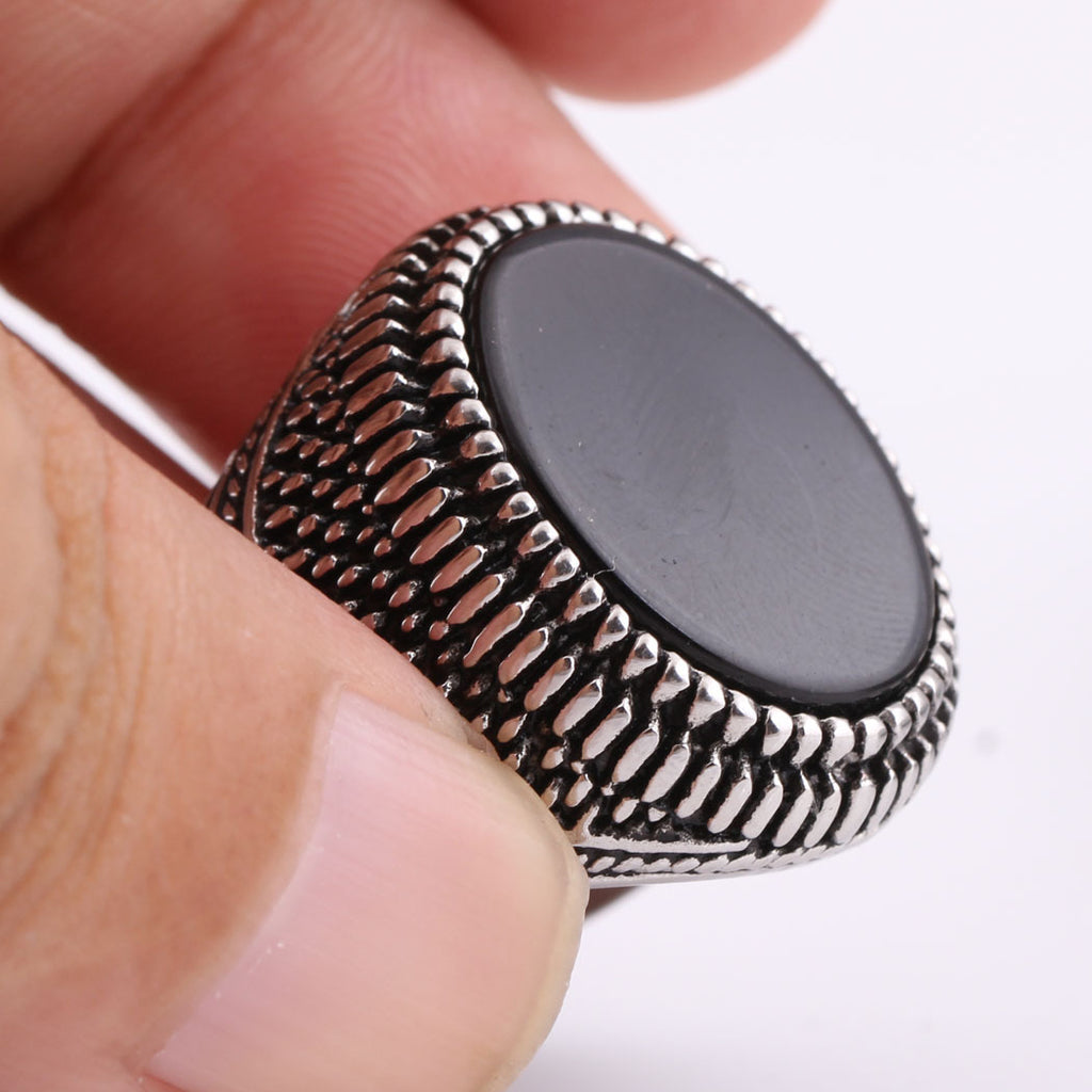 Silver ring with black stone held between fingers on a white background
