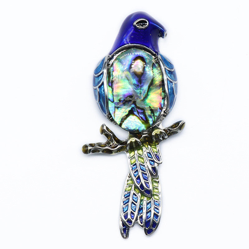 Colorful bird-shaped brooch with abalone shell center on a white background