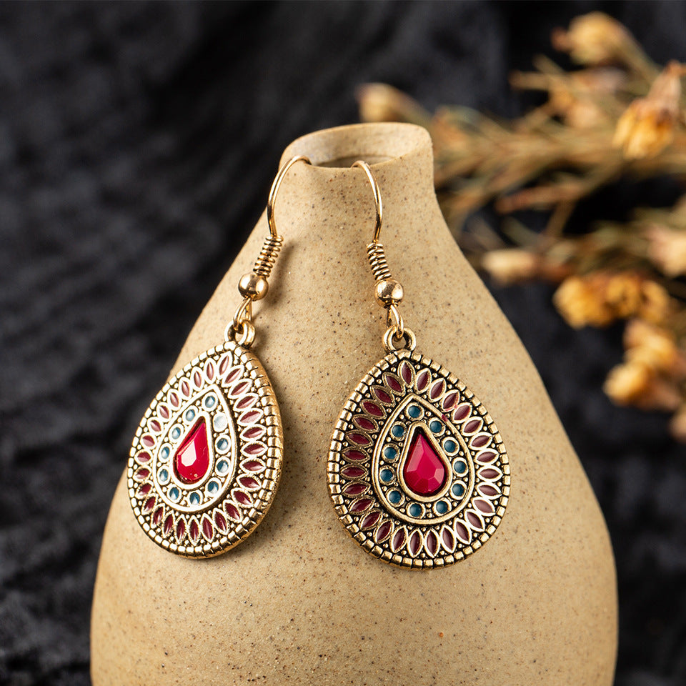Ornate earrings with red and blue stones on a beige stand against a dark background