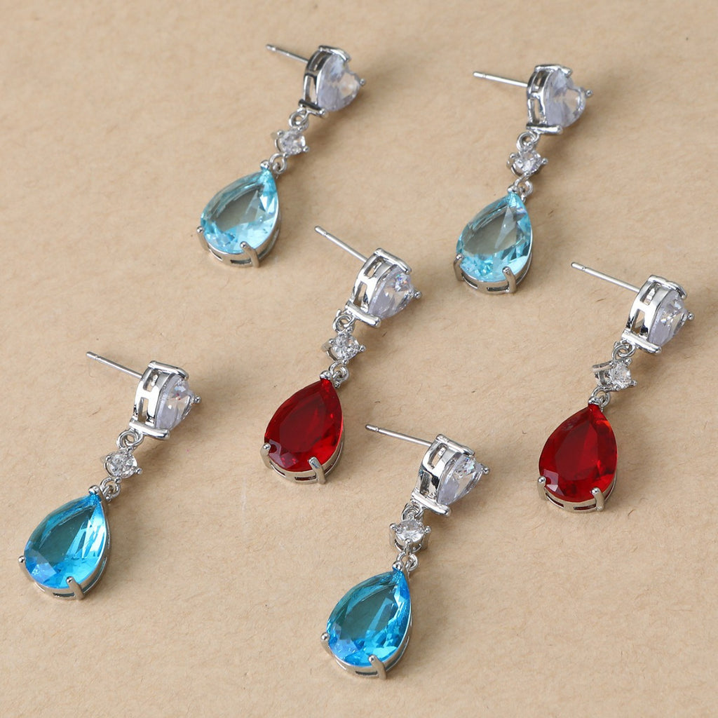 Set of teardrop-shaped earrings with blue and red gemstones on a beige background