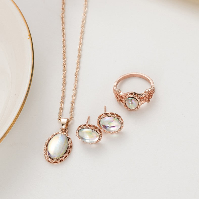 Rose gold jewelry set with pendant, earrings, and ring on a light background
