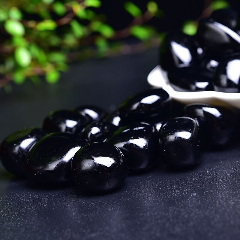 Black stones on a dark surface with a blurred green plant in the background