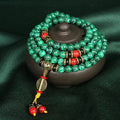 Green beaded bracelet with red and gold accents on a dark green fabric background