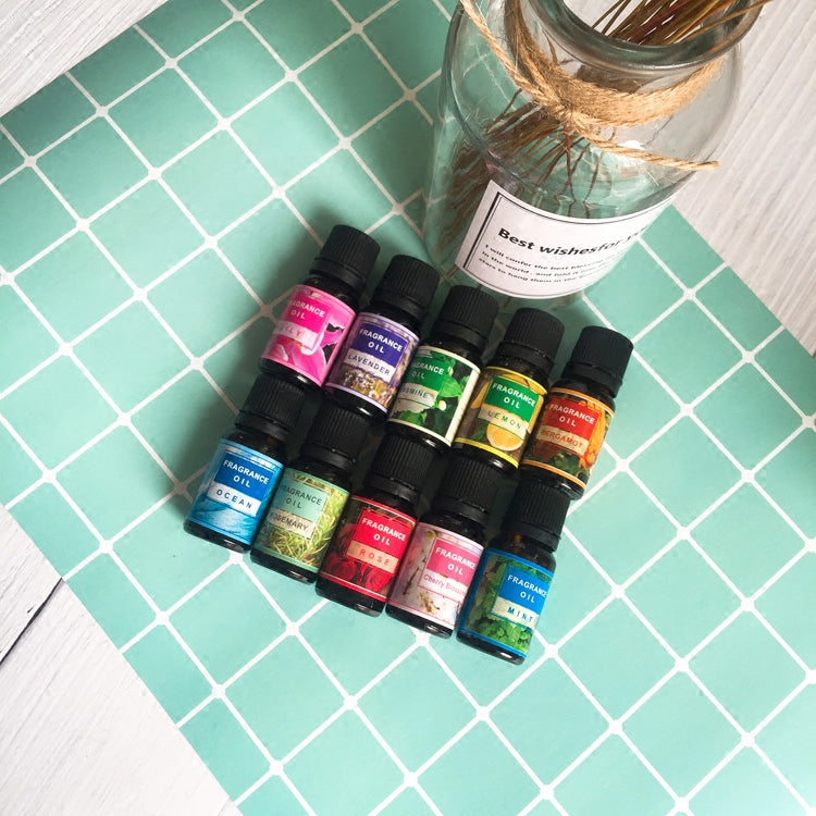 Collection of essential oil bottles on a green tiled surface with a glass jar labeled 'Best Wishes' in the background.