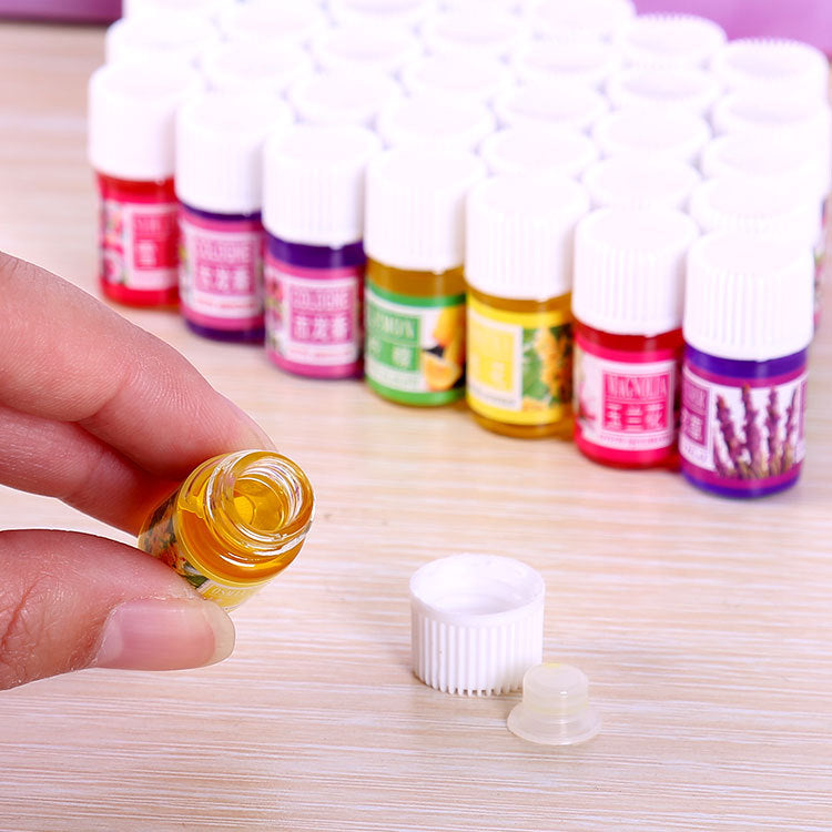 Hand holding a small bottle of yellow liquid with other similar bottles in the background on a wooden surface.