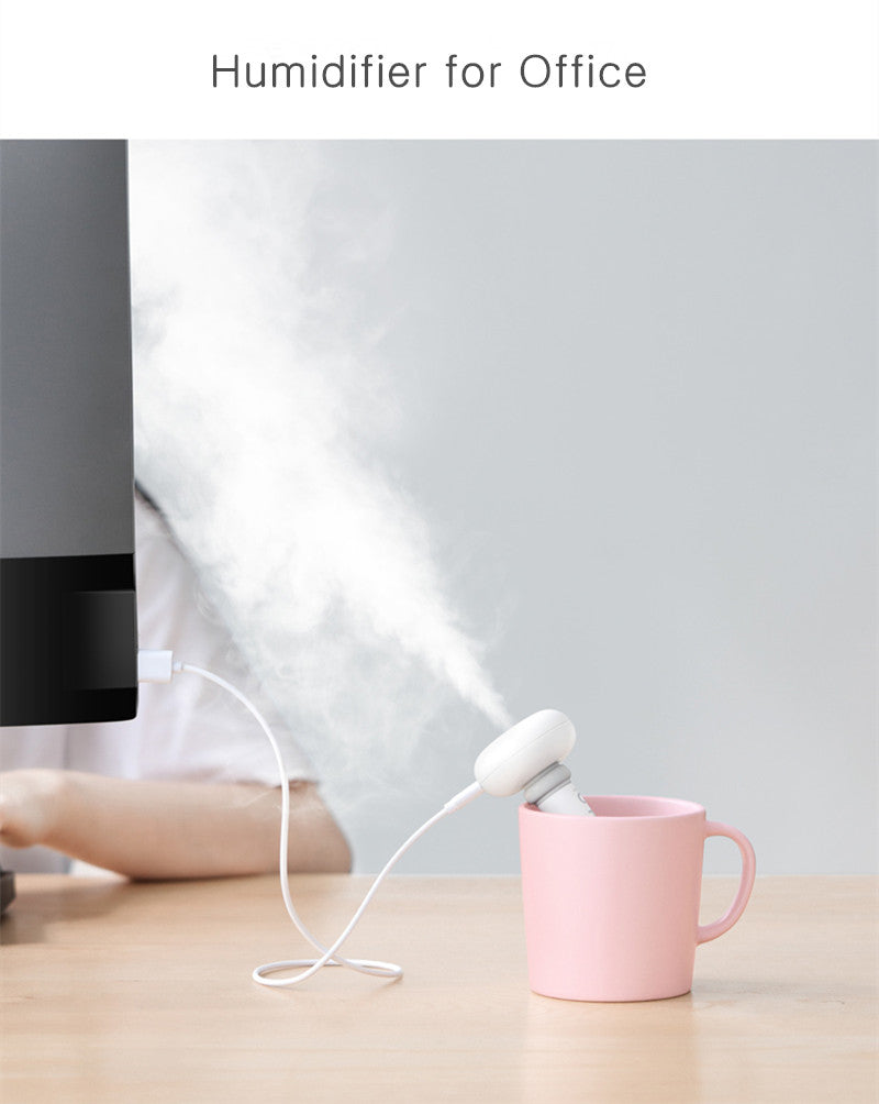 Humidifier emitting steam into a pink mug on a desk with a computer monitor in the background.