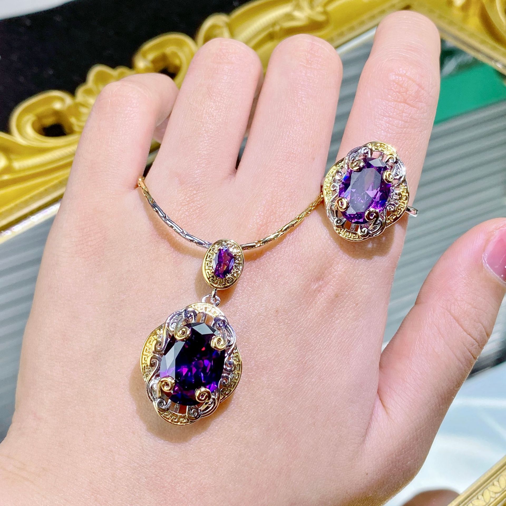 Hand wearing a gold bracelet with purple gemstones in front of a decorative mirror.