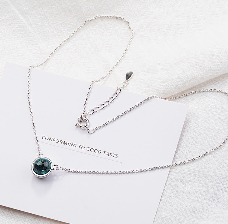 Silver necklace with a green gemstone on a white card