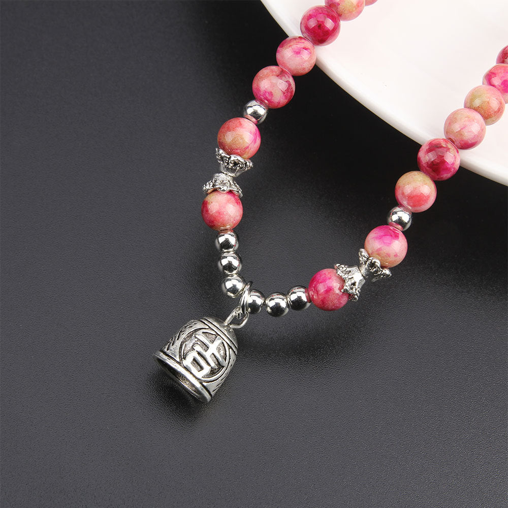Bracelet with pink beads and a silver charm on a dark surface