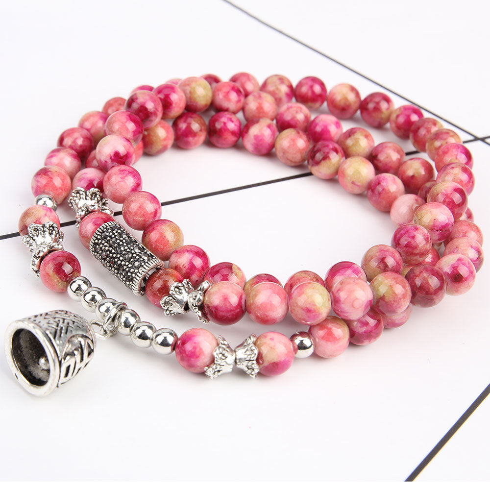 Pink beaded bracelet with silver charms on a white background