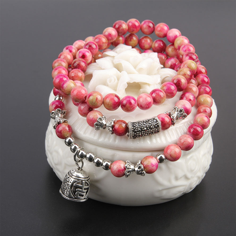 Pink beaded bracelets with silver charms on a white decorative object against a dark background