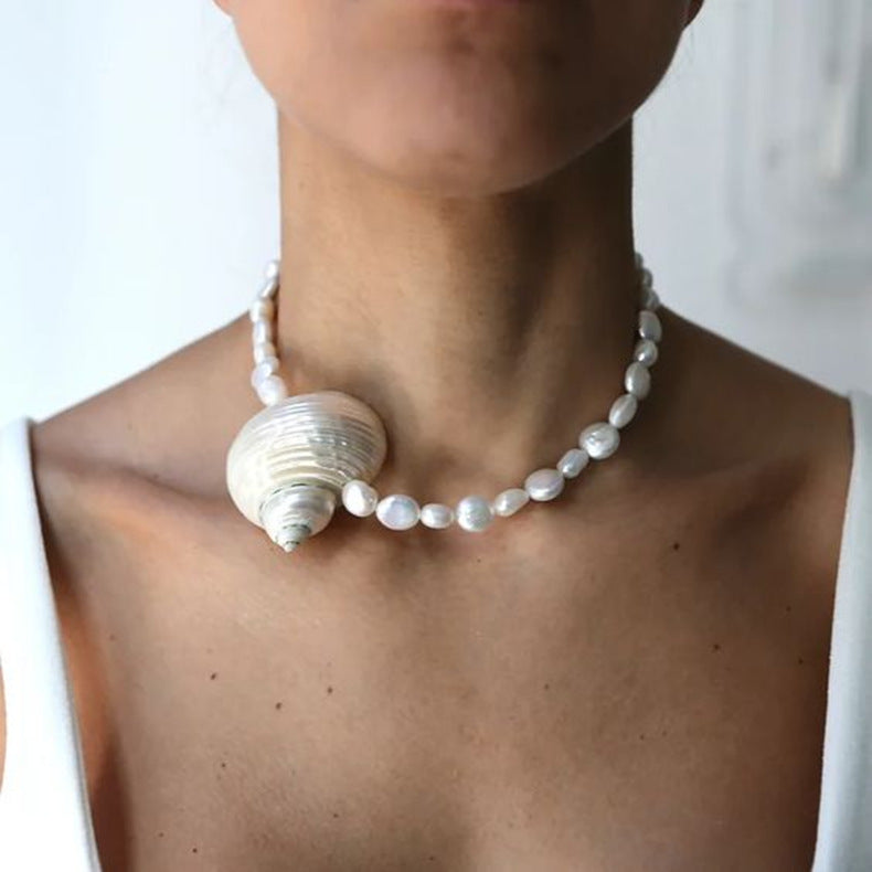 Pearl necklace with seashell accents worn by a person against a white background