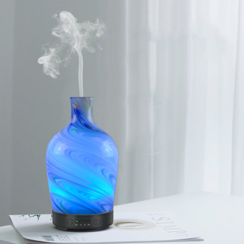 Blue glass diffuser emitting mist on a white surface with a gray curtain background