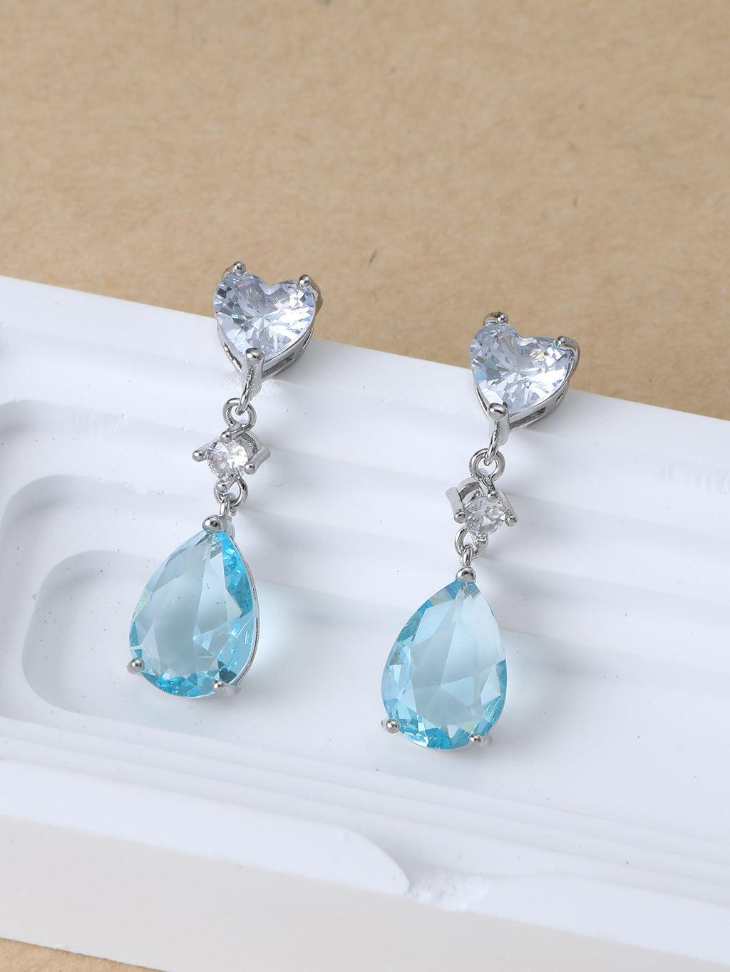Pair of earrings with heart and teardrop-shaped blue gemstones on a beige background