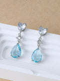 Pair of earrings with heart and teardrop-shaped blue gemstones on a beige background
