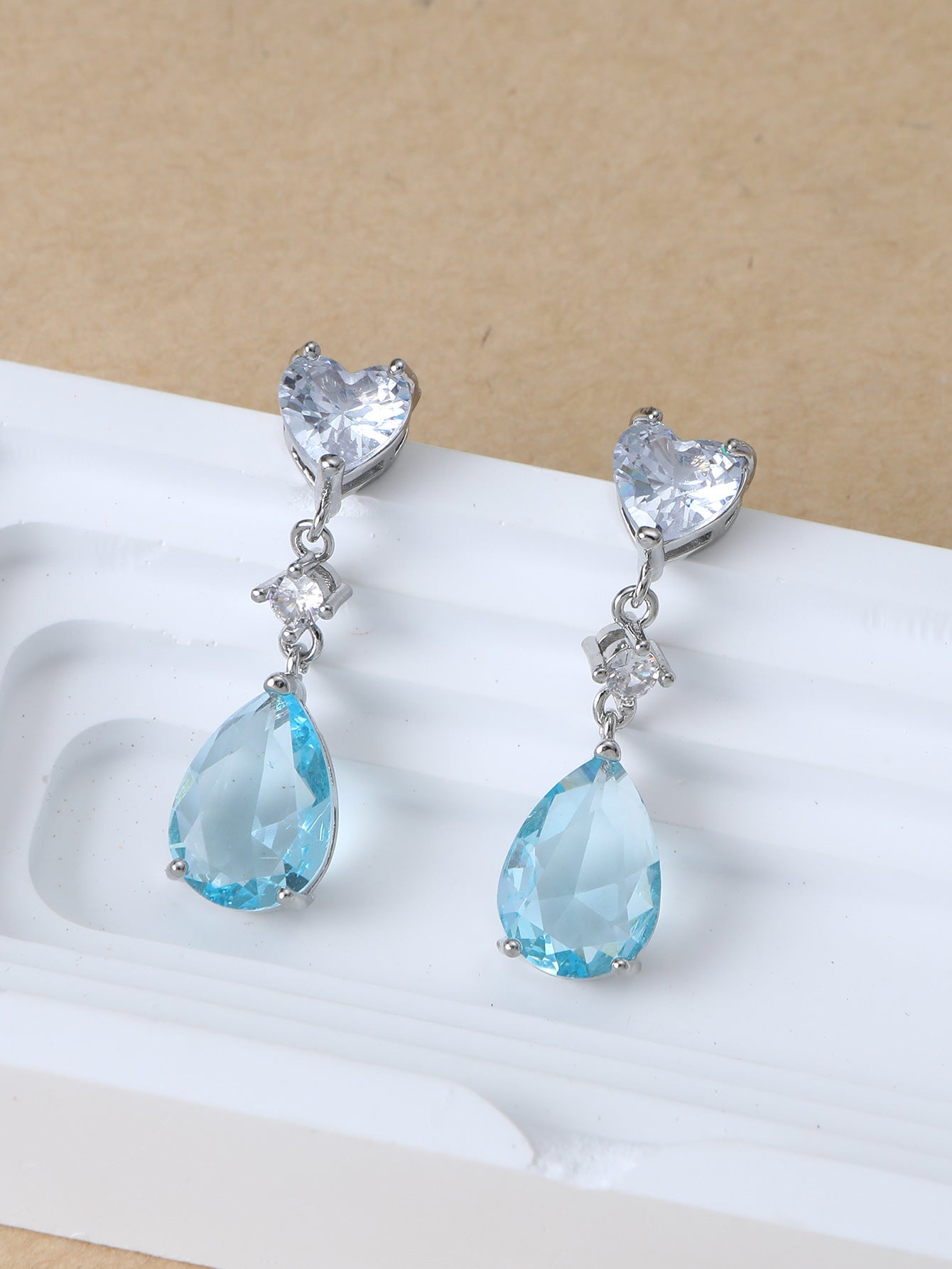 Pair of earrings with heart and teardrop-shaped blue gemstones on a beige background