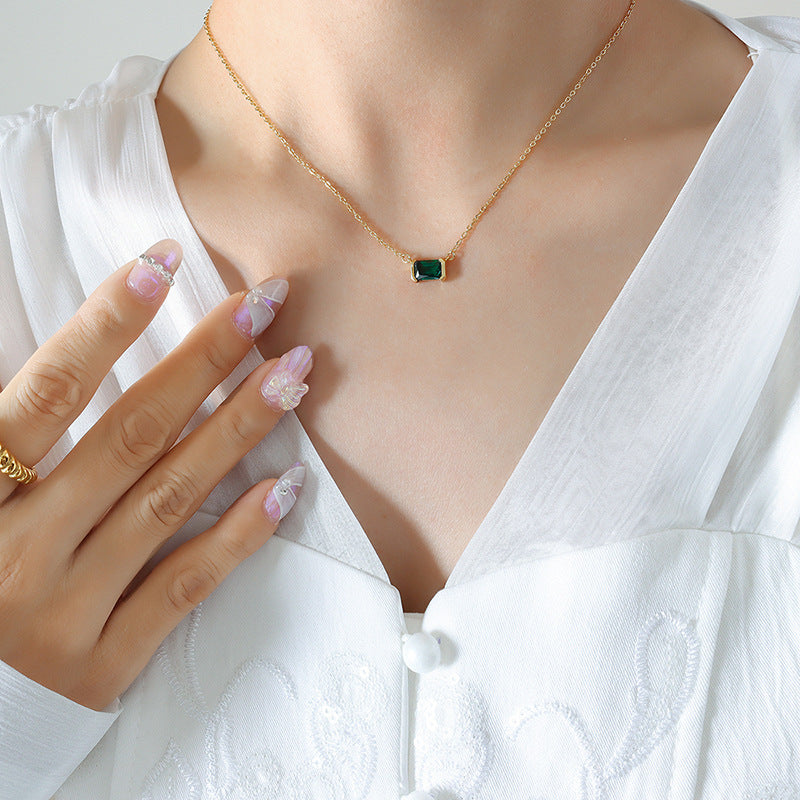 Gold necklace with a green gemstone worn by a person in a white outfit.