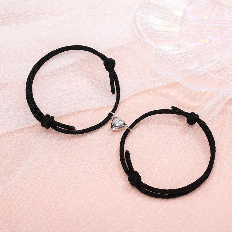 Two black bracelets with heart-shaped charms on a light pink surface.