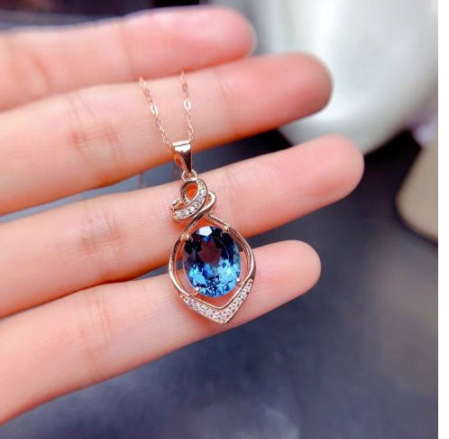 Rose gold necklace with a blue gemstone pendant held in a hand.