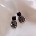 Pair of silver earrings with black gemstones on a light pink fabric background