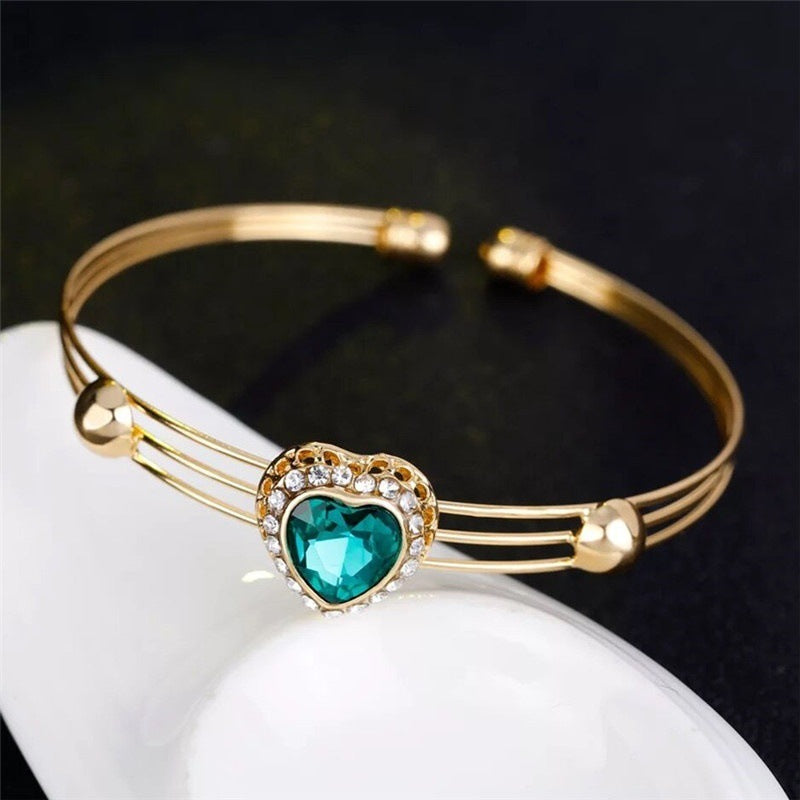 Gold bracelet with a heart-shaped green gemstone on a white surface