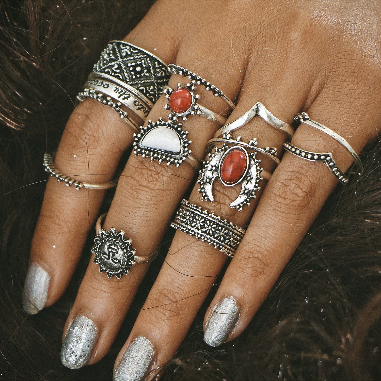 Close-up of a hand wearing multiple silver rings with gemstones on a dark background