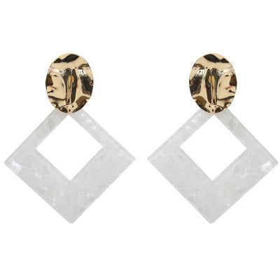 Pair of earrings with gold round stones and white square bases on a white background