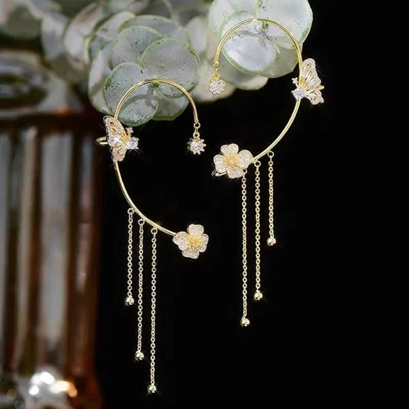 Gold hoop earrings with floral and butterfly designs against a dark background