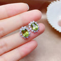 Green gemstone earrings held between fingers on a neutral background