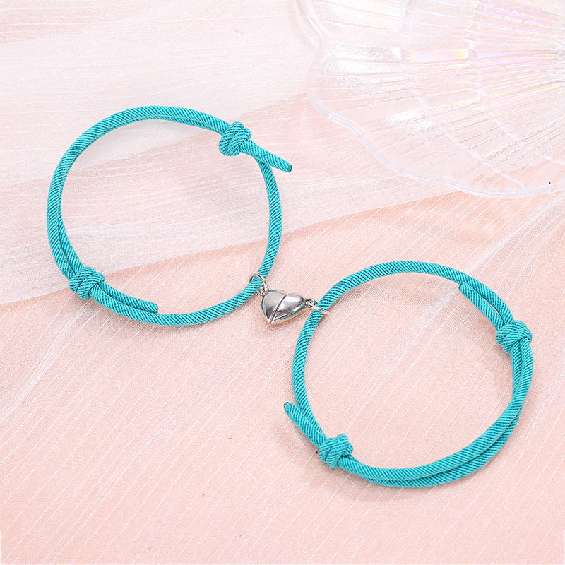 Turquoise cord bracelet with a silver heart charm on a light pink surface