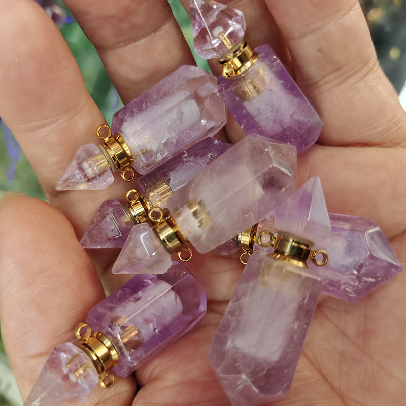 Hand holding multiple small crystal bottles with gold caps against a blurred natural background