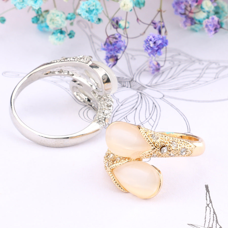 Two rings, one silver and one gold with a heart-shaped stone, on a white surface with decorative elements.
