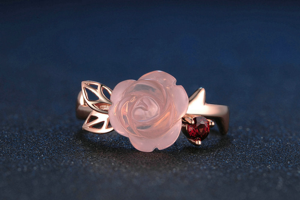 Rose gold ring with a pink rose design and red gemstone on a dark background