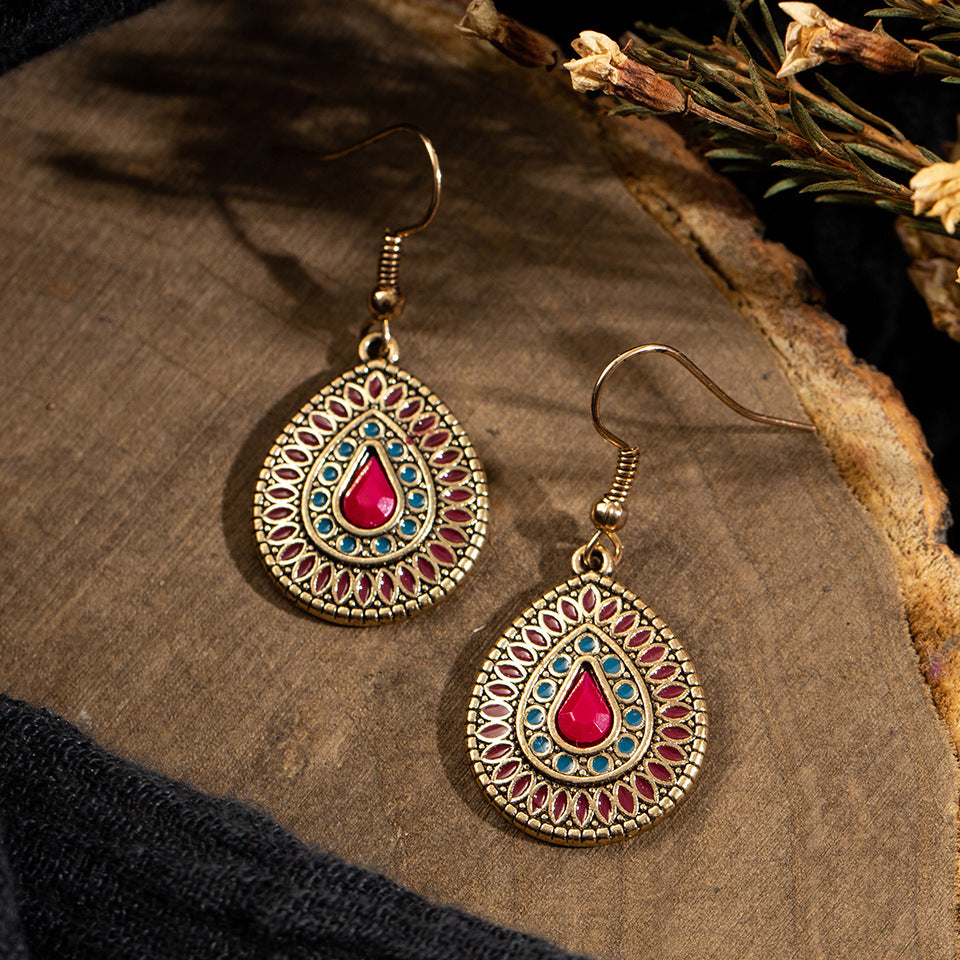 Teardrop-shaped earrings with red gemstones on a wooden surface