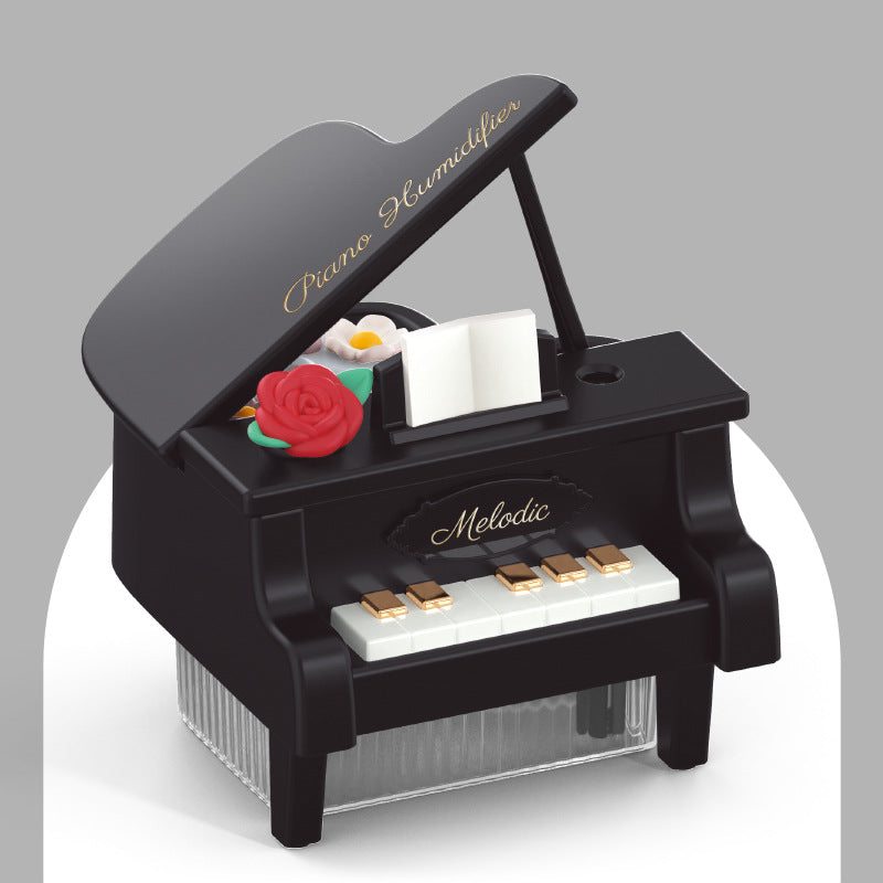 Small black piano-shaped toy with a red rose and sheet music on a gray background