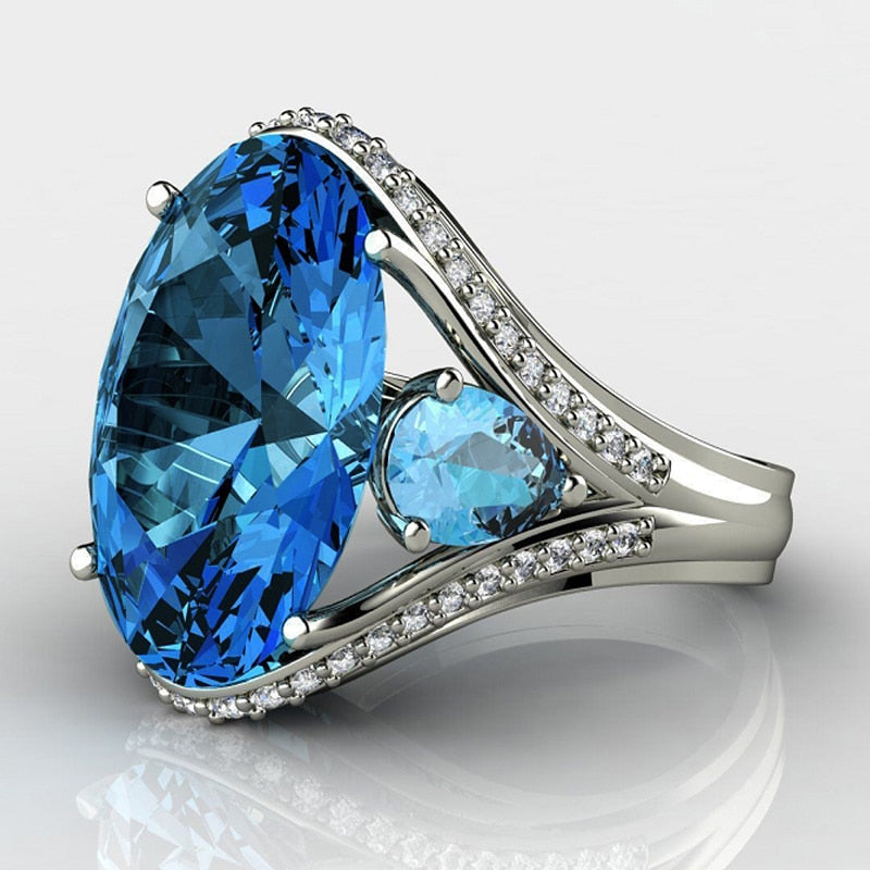 Silver ring with a large blue gemstone and smaller diamonds on a white background
