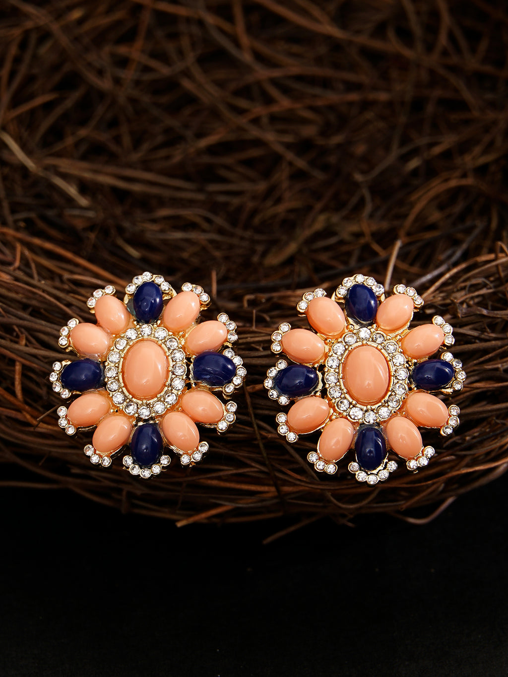 Pair of floral earrings with coral and blue stones on a dark background
