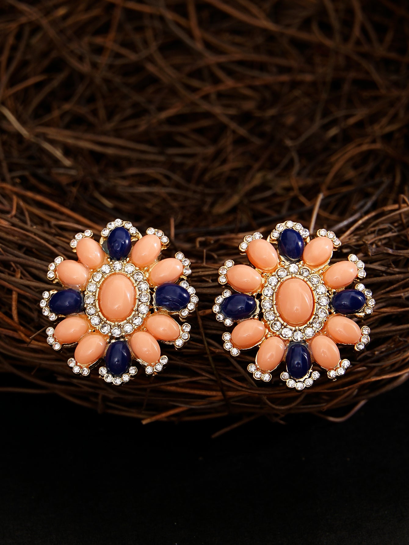 Pair of floral earrings with coral and blue stones on a dark background