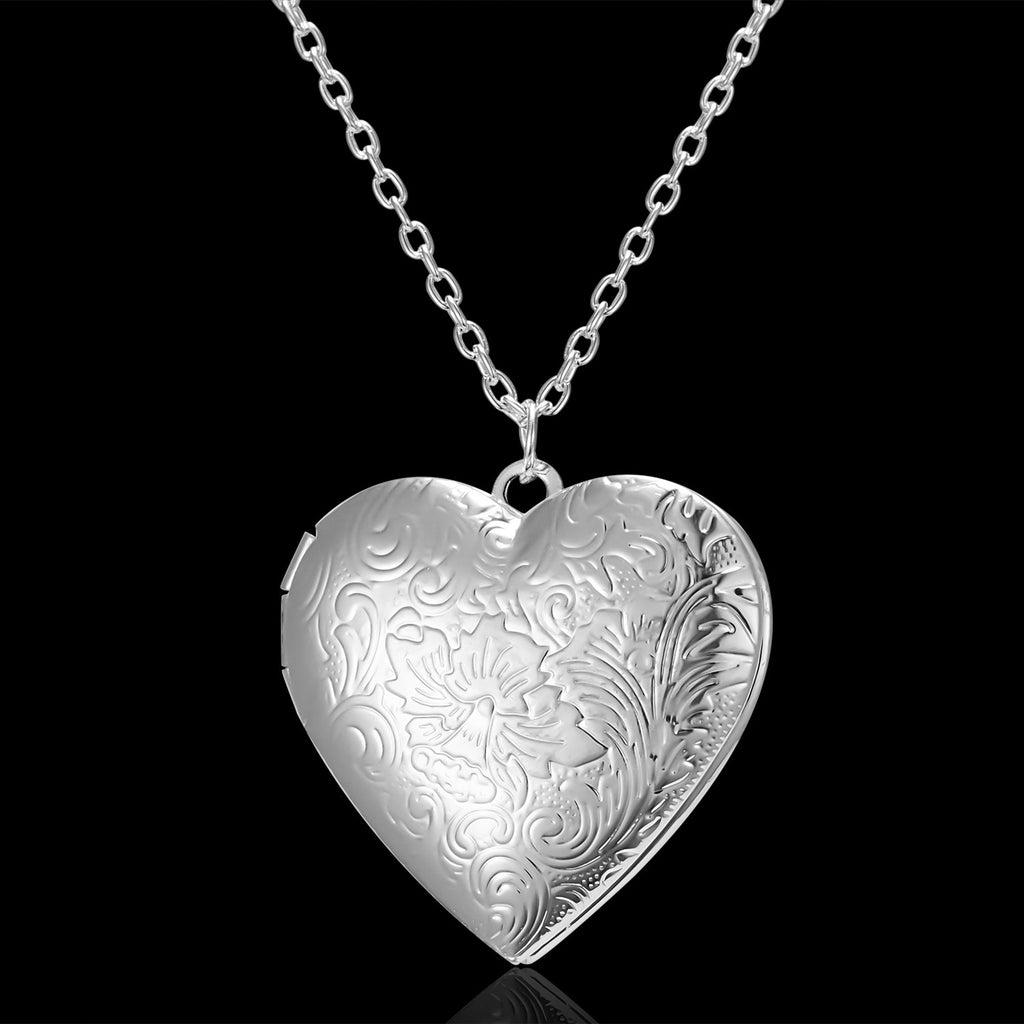 Silver heart-shaped locket with intricate designs on a black background