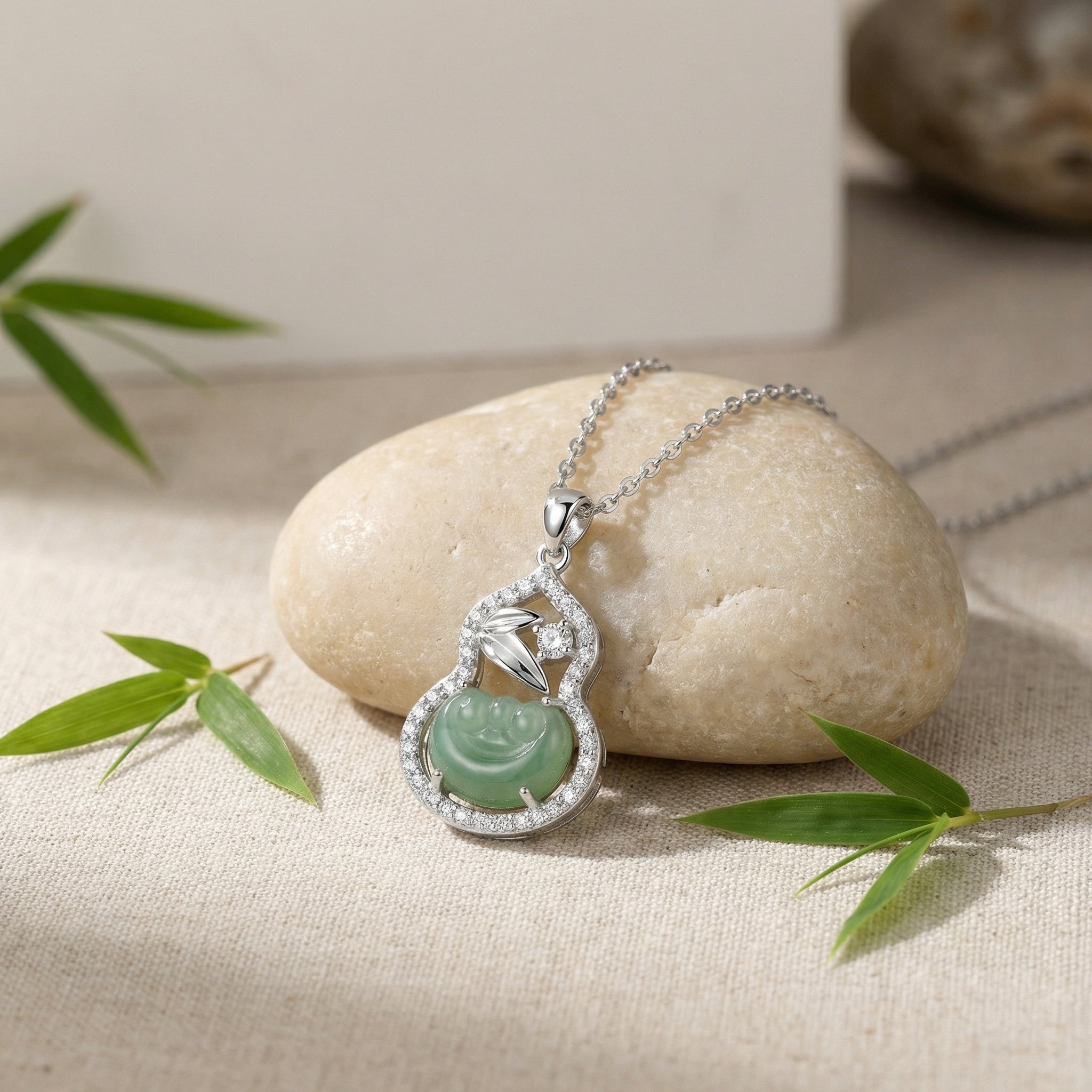 Silver necklace with a green pendant on a stone surface with bamboo leaves