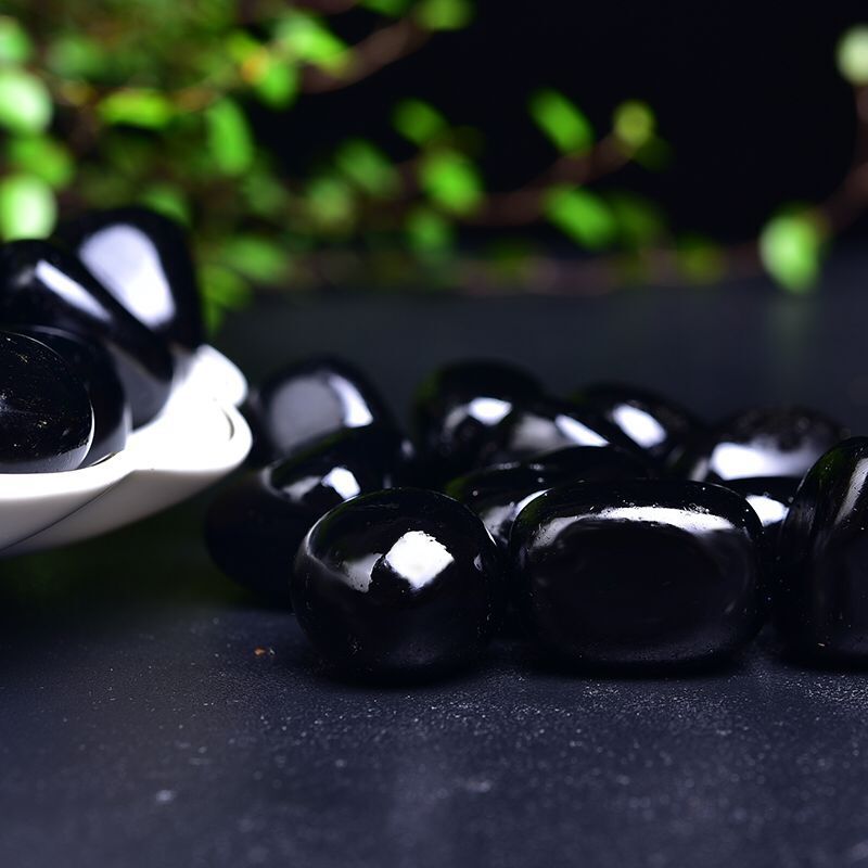 Black stones on a dark surface with a blurred green plant in the background