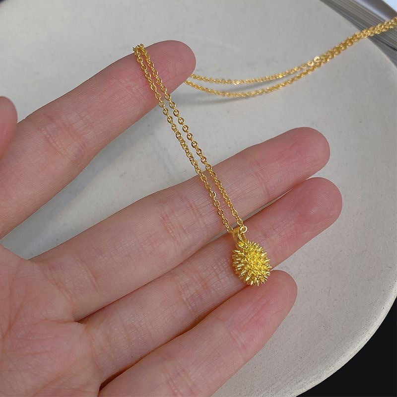 Gold necklace with a small pendant held between fingers on a neutral background