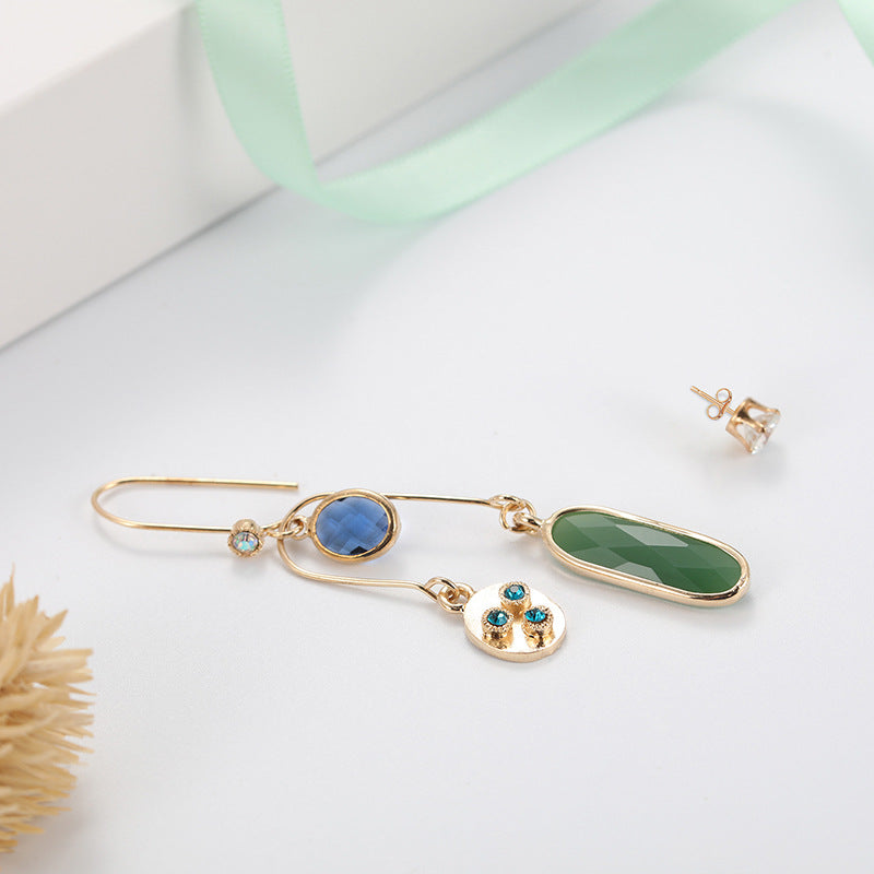 Gold earrings with green and blue stones on a white background